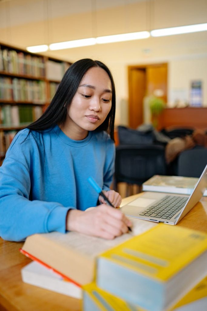 Focused young woman studying and writing notes with a laptop for online academic writing help